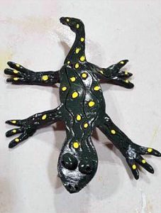 A glossy thin ceramic sculpture of a green lizard with yellow spots
