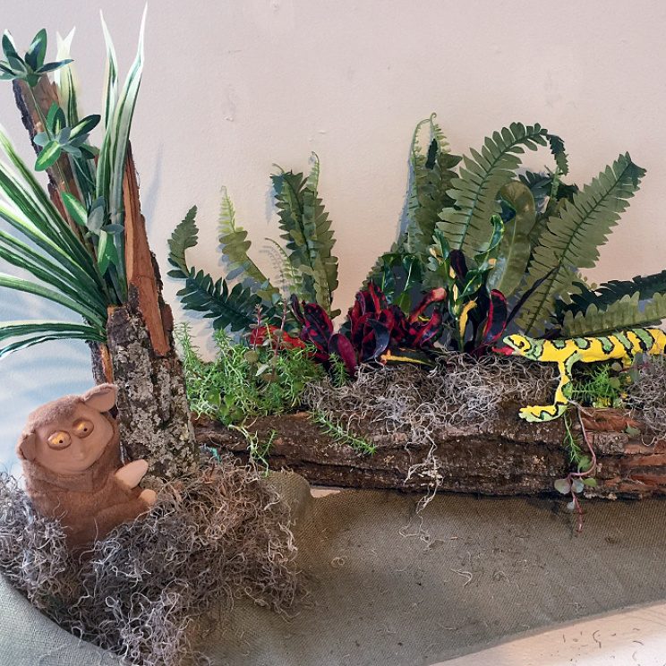 Frontispiece, floral and plant arrangement with wood log planter, ceramic lizard, and ceramic tarsier monkey.