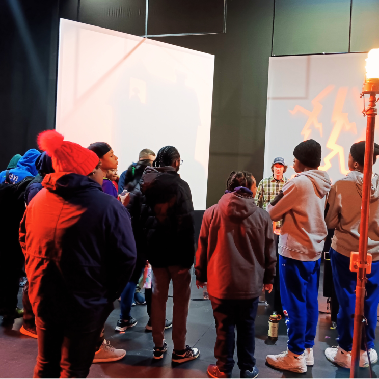 a group of students stand in a circle in a back stage area of a theater