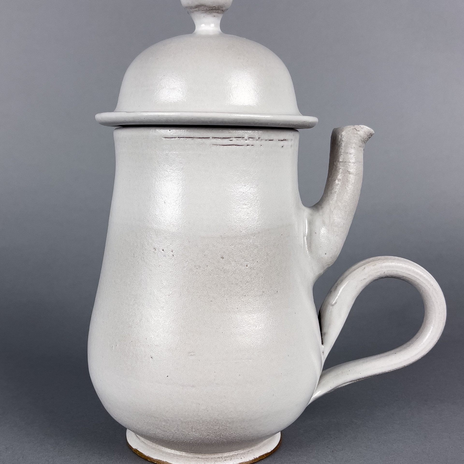 Non-Functional_11 A tall white teapot. The curved handle for the teapot is located directly below the spout. The spout sticks straight up into the air. Both of these factors make pouring the tea an awkward endeavor.